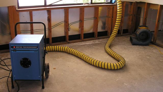 Dehumidifier with a yellow duct drying a room with open wall cavities